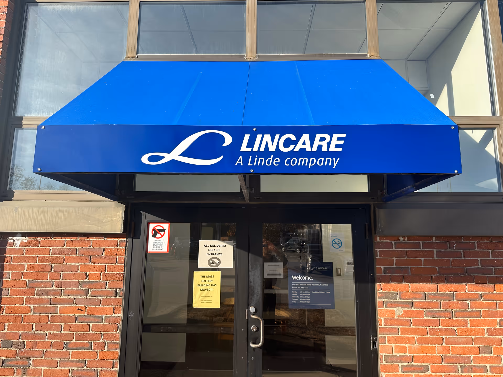 Blue awning with LINCARE sign over glass entrance door to brick exterior building.