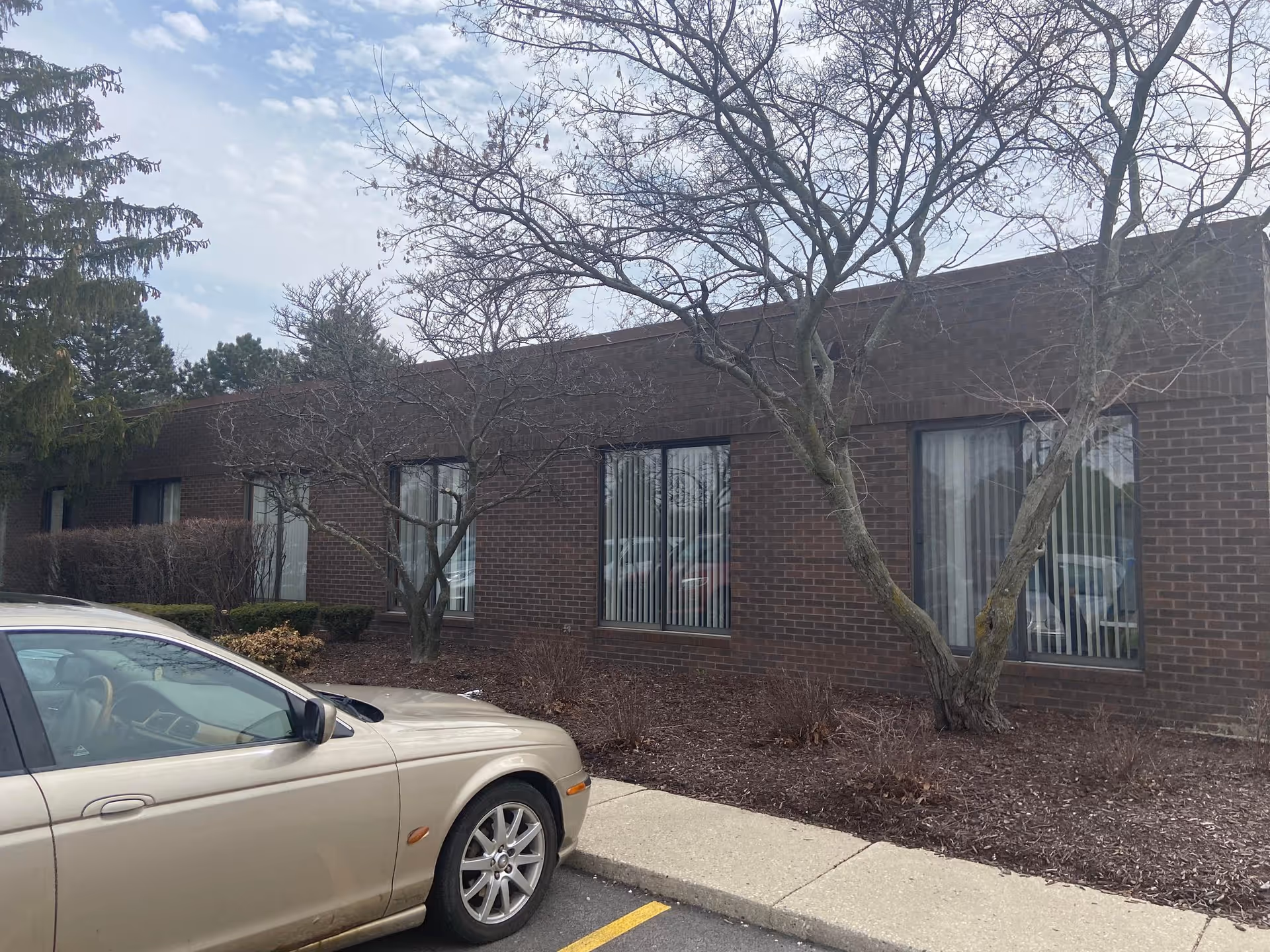 Brick Home Instead facility exterior with large windows, leafless trees, and a parked beige car.