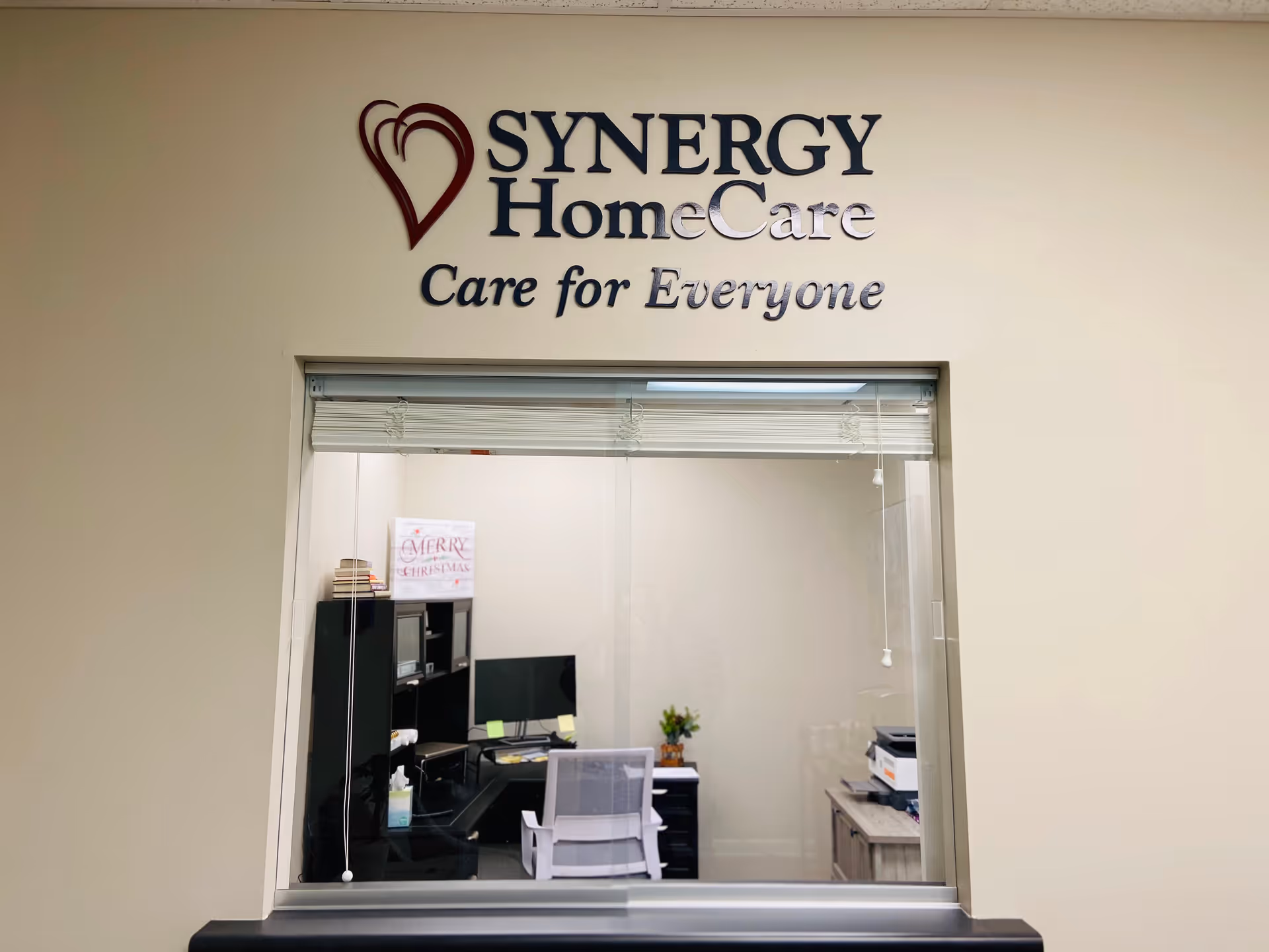 Interior reception area with SYNERGY HomeCare sign and office workspace behind glass