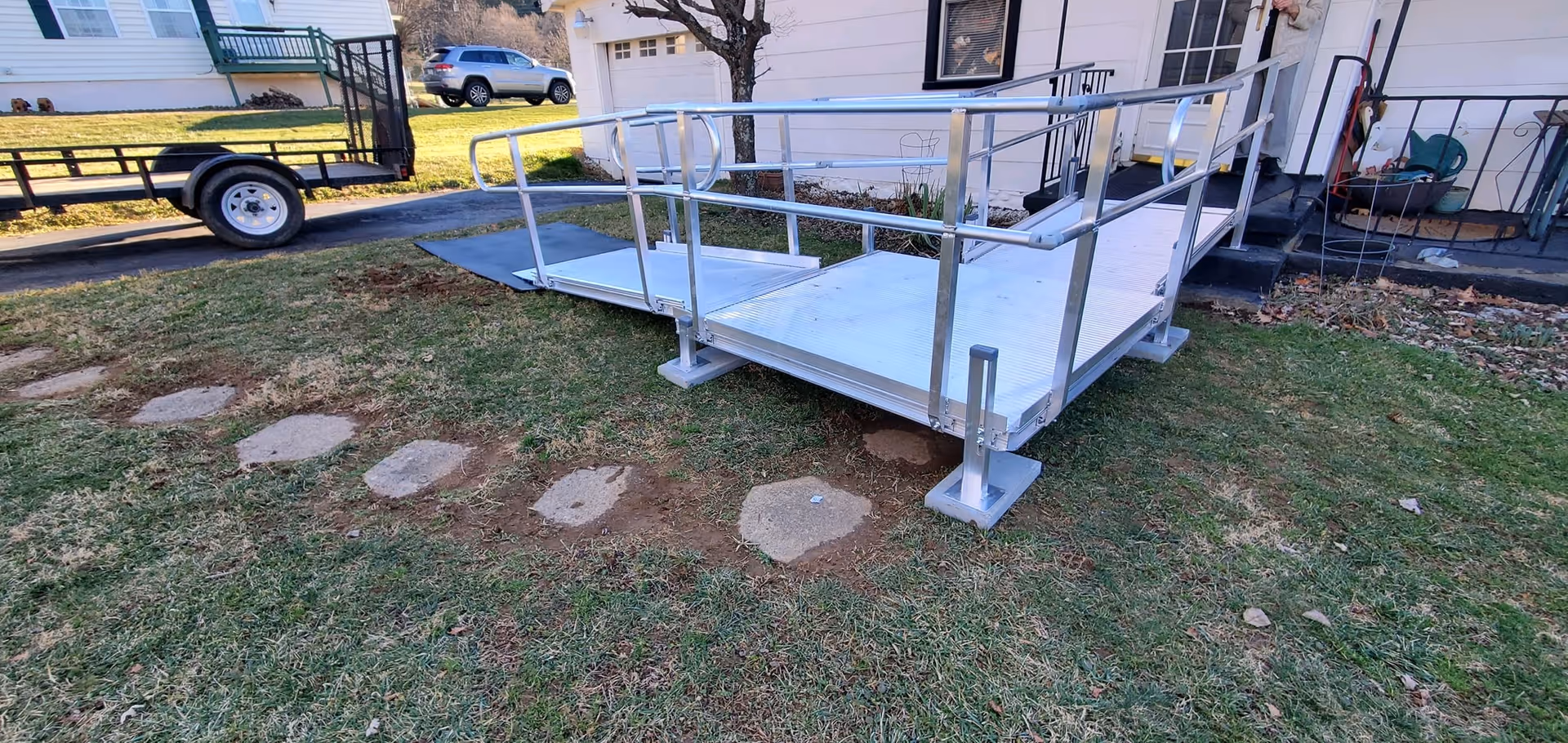Aluminum wheelchair ramp with handrails extends from a house entrance to a grassy yard.