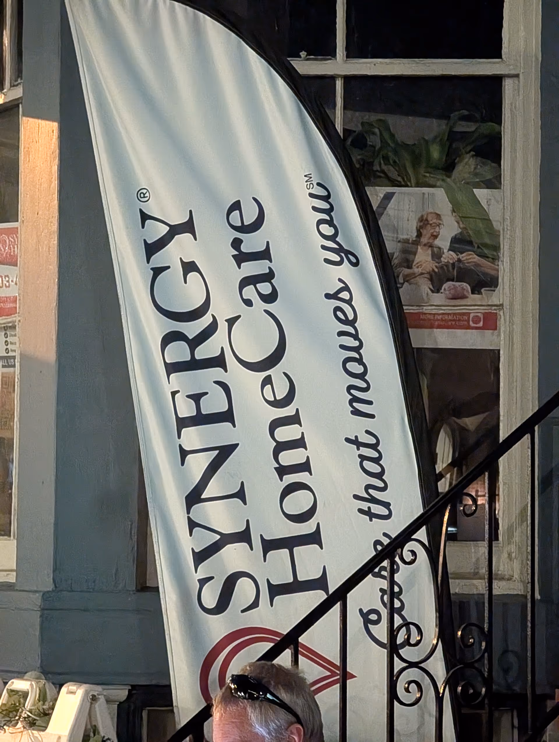 Exterior building front with a vertical Synergy HomeCare banner beside steps.