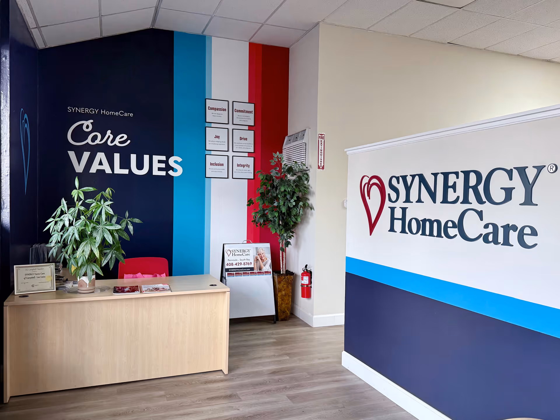 Reception area featuring SYNERGY HomeCare branding, a desk, plants, and core values wall.