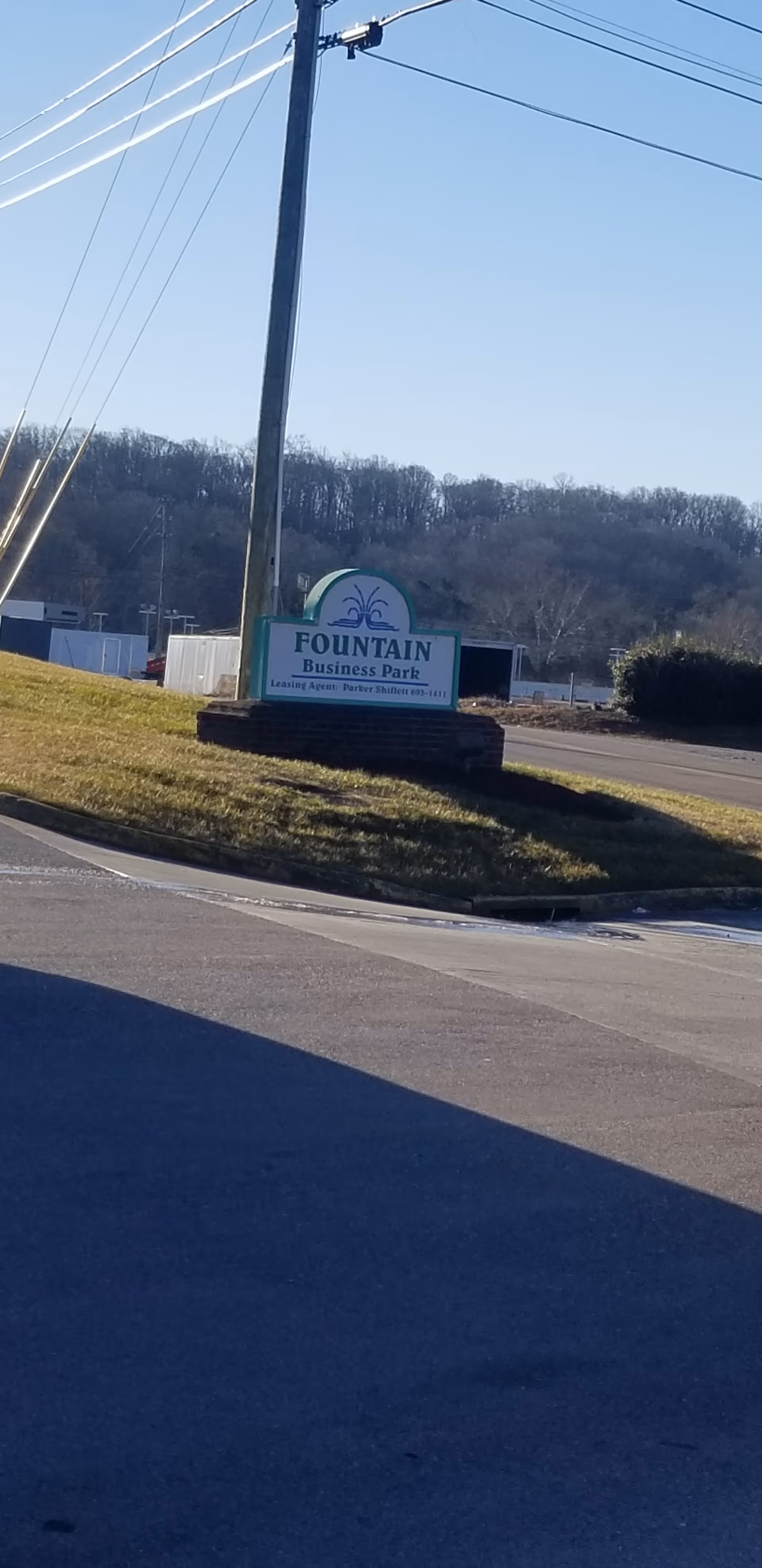 Roadside sign for Fountain Business Park on a grassy median with power lines overhead.