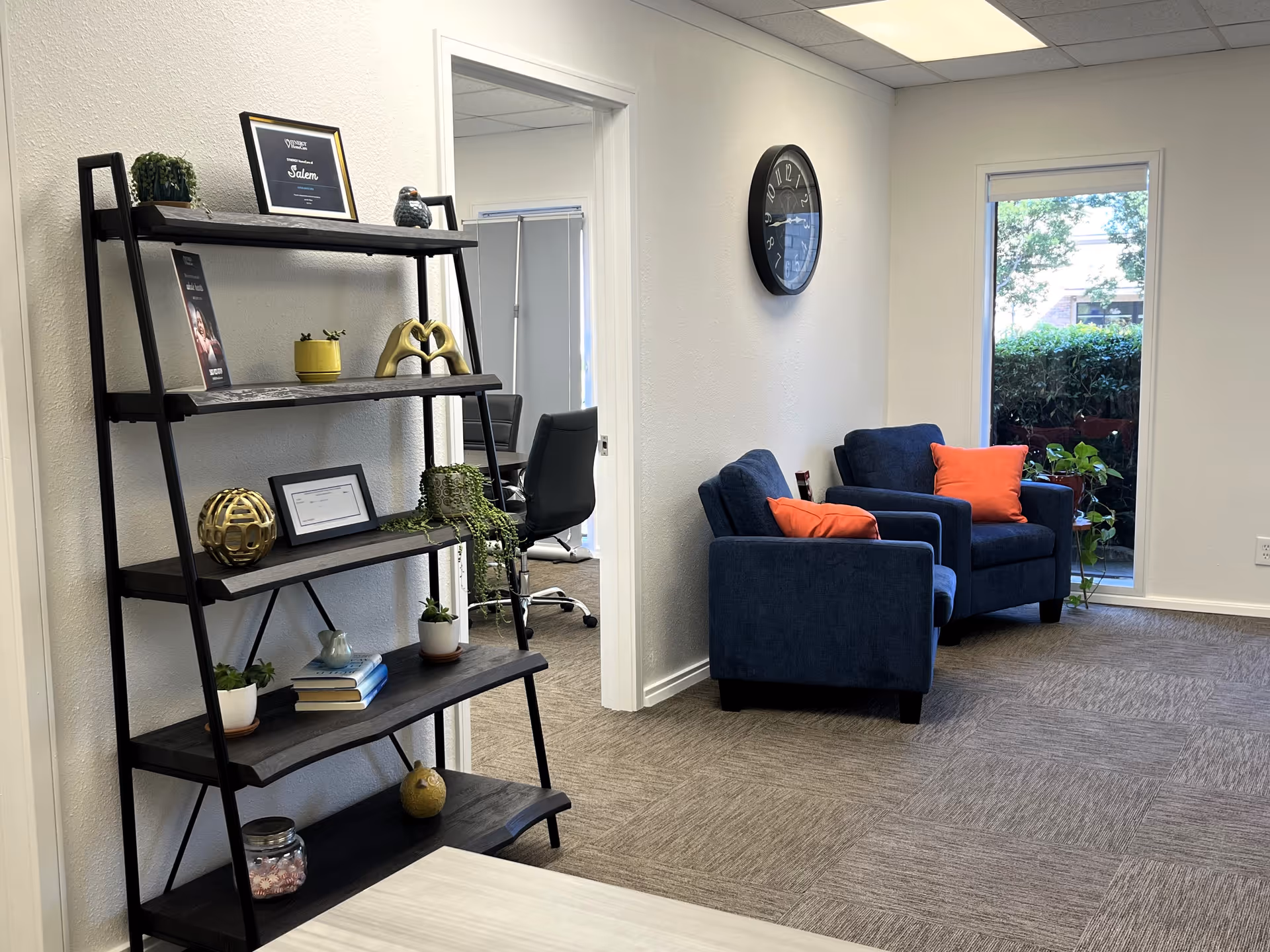 Blue armchairs with orange pillows beside a window in a waiting lounge.