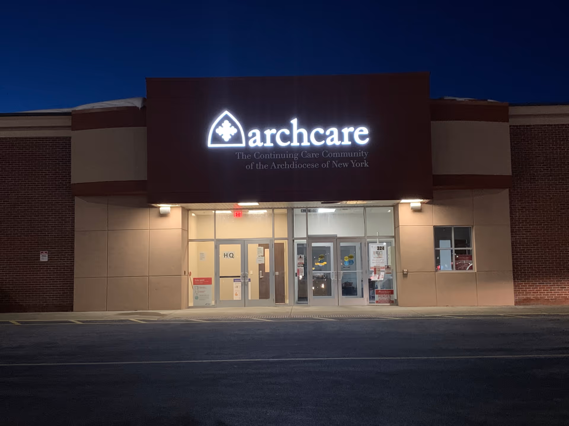 Nighttime exterior of ArchCare at Home building with illuminated sign and glass doors.
