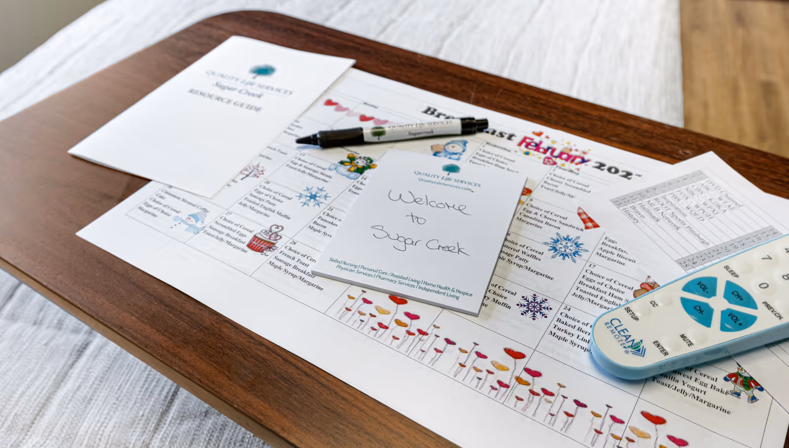 Desk with papers, a pen, remote, and welcome card in an interior facility setting.