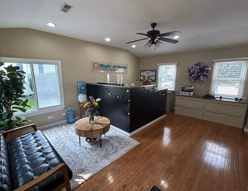 Reception area with black-front desk, sign, seating, water cooler, and large windows.
