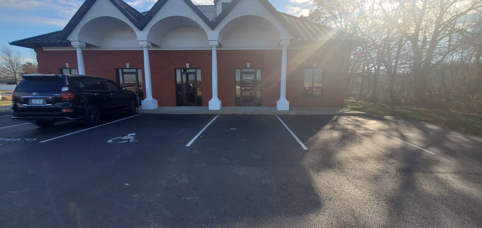 Brick facility front with arches, glass doors, white columns, and a parking lot.