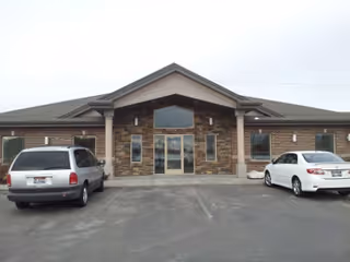 Brick building with central glass entrance and two parked cars in front.