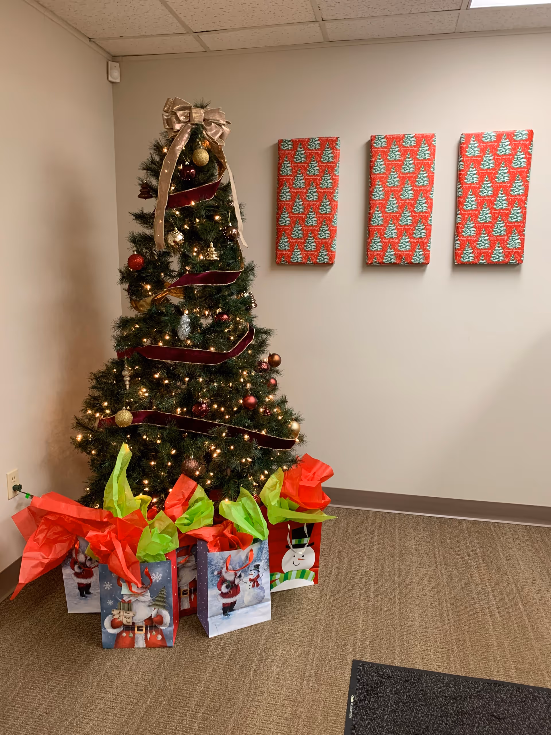 Decorated Christmas tree with gift bags stands in a hallway at AdvisaCare Home Health & Hospice.