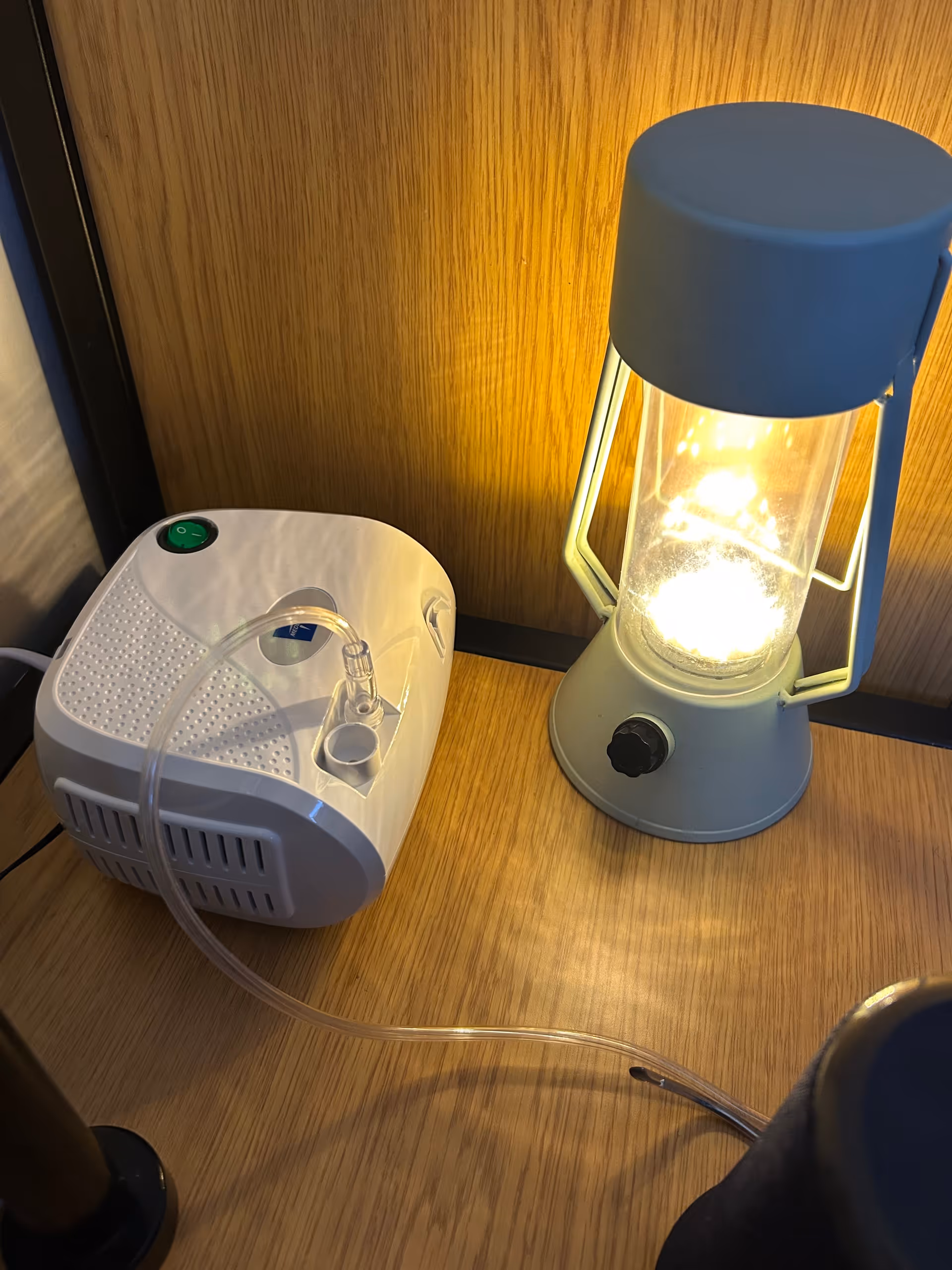 Bedside table with blue lantern lamp and compact medical device on wood surface.