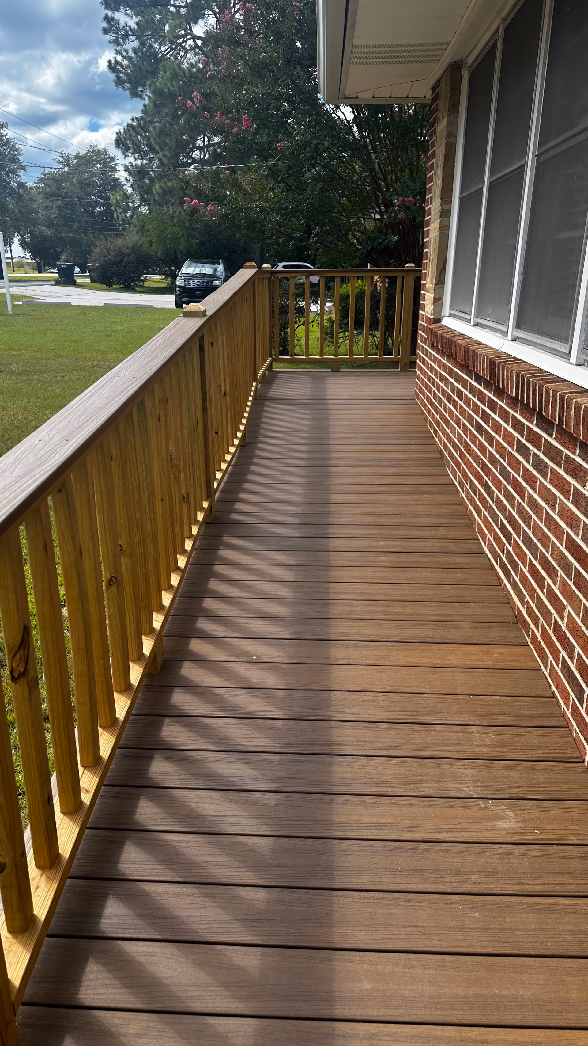 A wooden outdoor deck along a brick building with railing and windows.