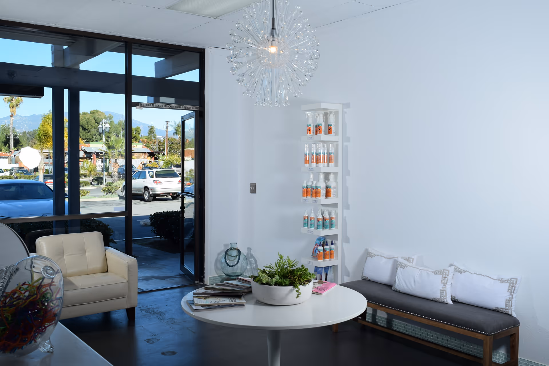 Modern lobby seating area with a round table and product shelves near glass doors.
