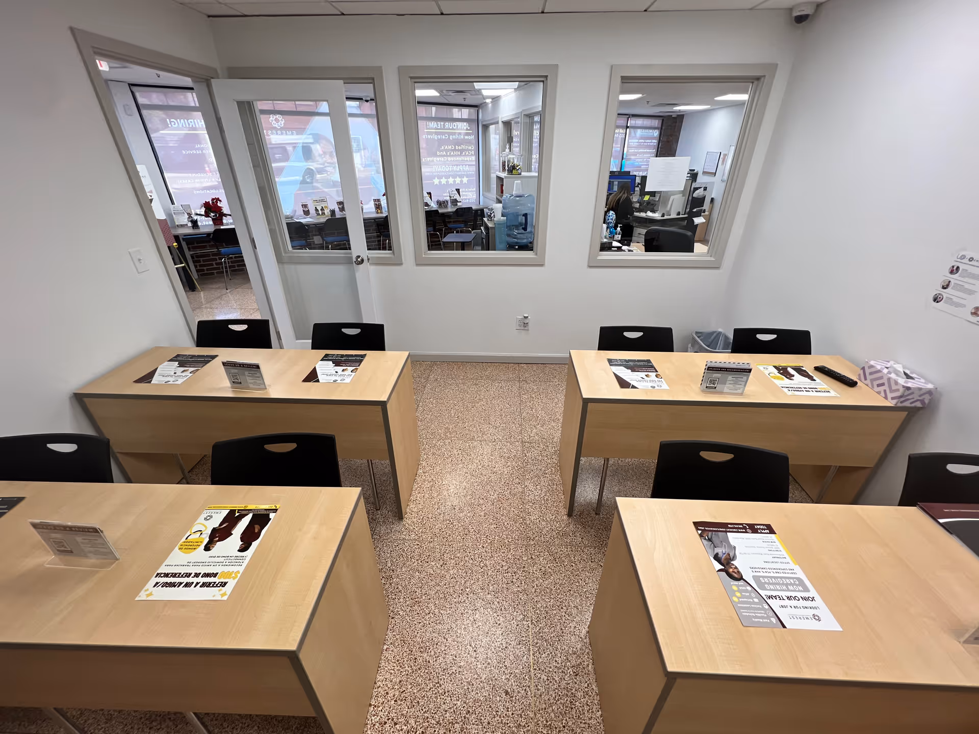 Empty classroom-style reception area with wooden desks, chairs, and brochures visible.