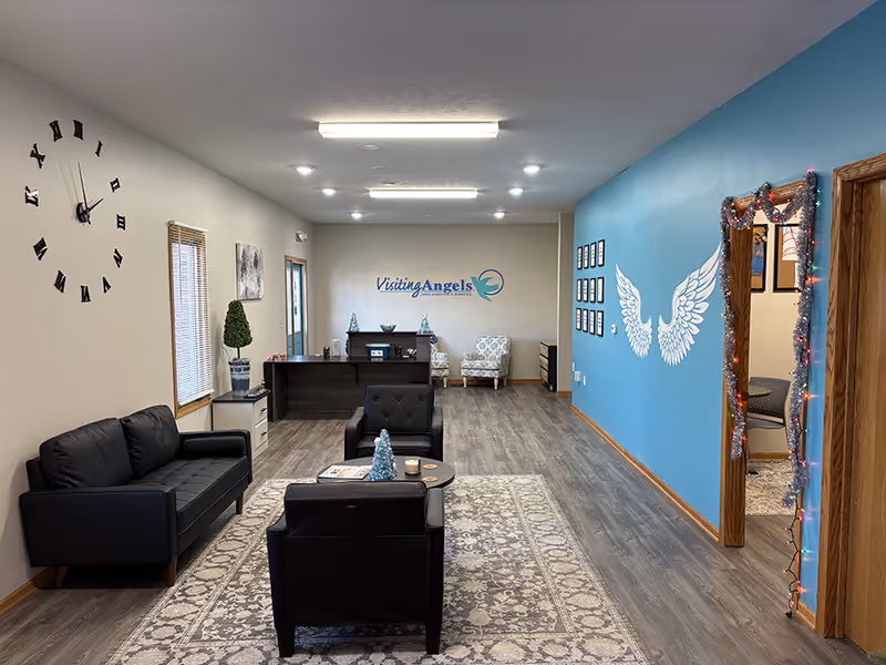 Reception area with black sofas, a gray rug, and a blue wall mural of angel wings.