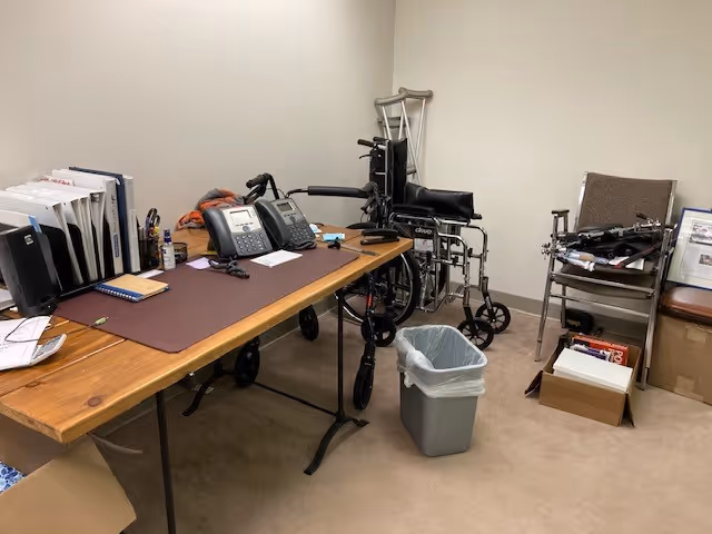 Office workspace with desk, supplies, and medical equipment including wheelchair and walker.