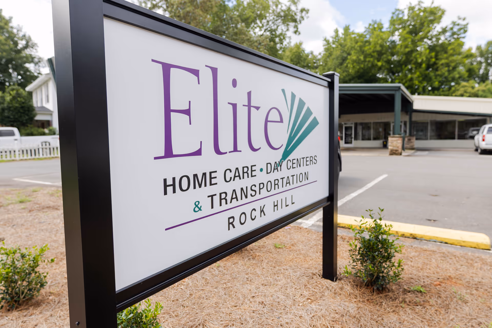 Outdoor sign for Elite Home Care Day Centers & Transportation near a parking lot.
