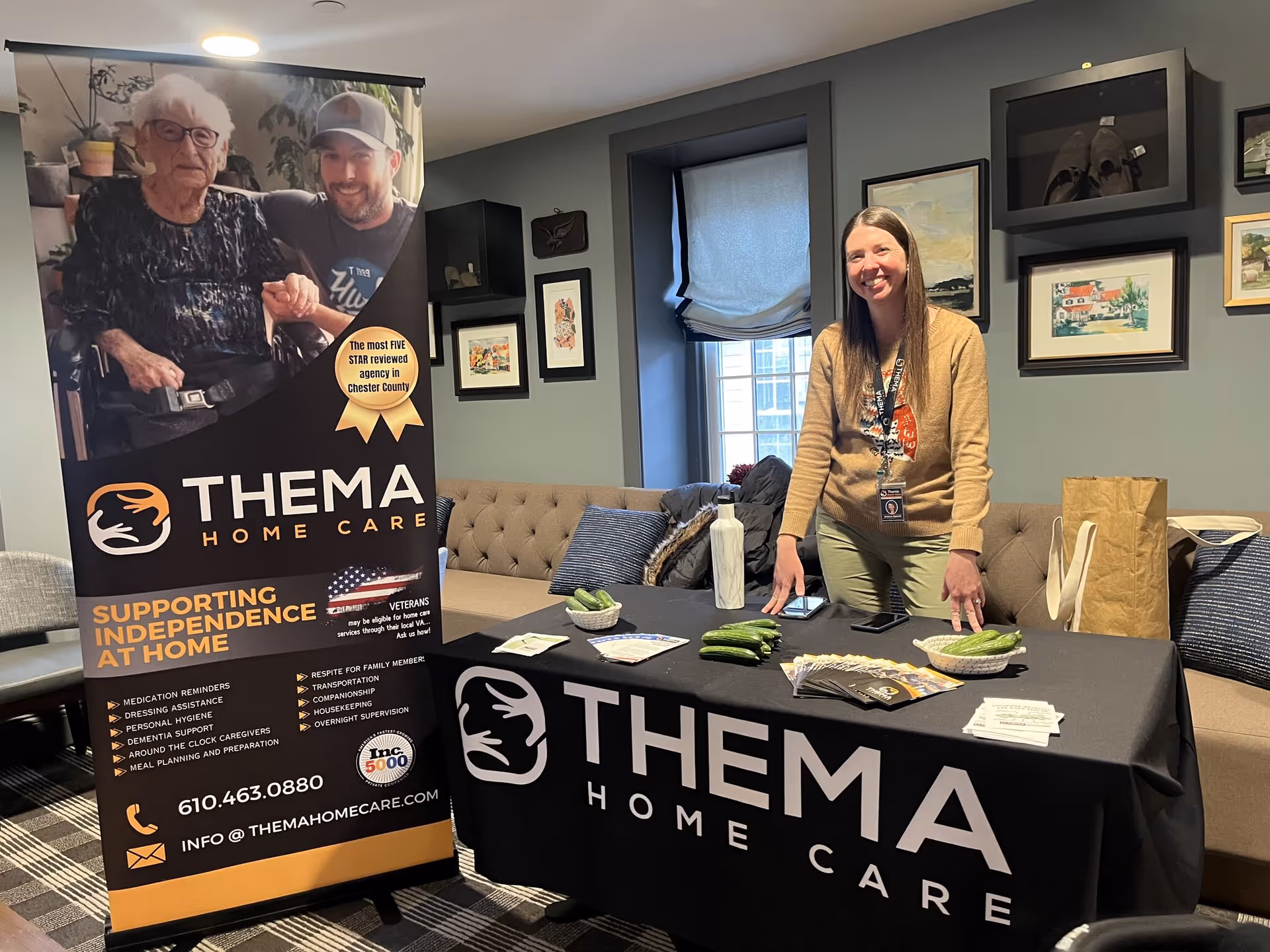 Indoor lounge with Thema Home Care banner and a smiling staff member behind a promotional table.