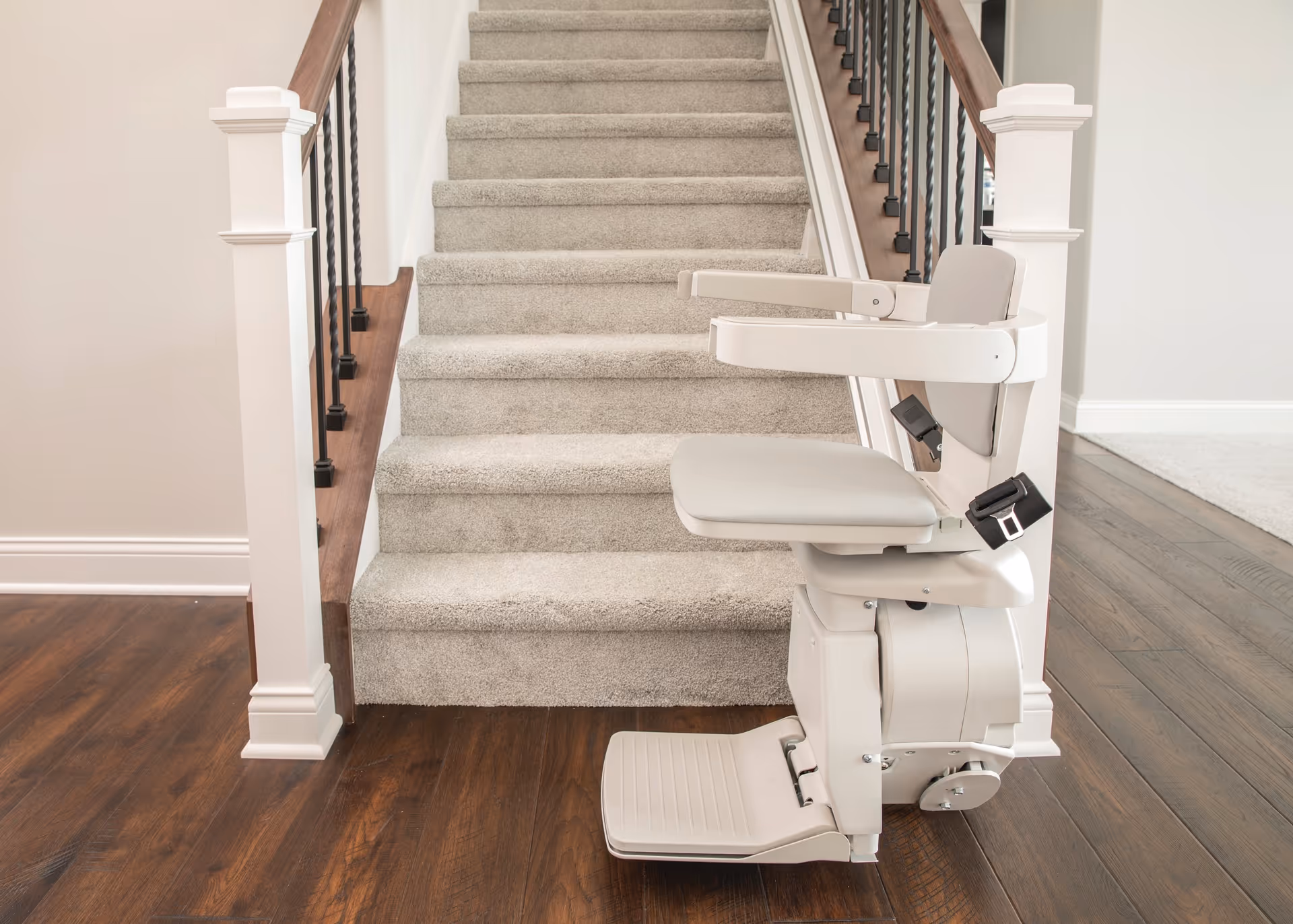 A white stair lift is installed beside a carpeted staircase in an interior.