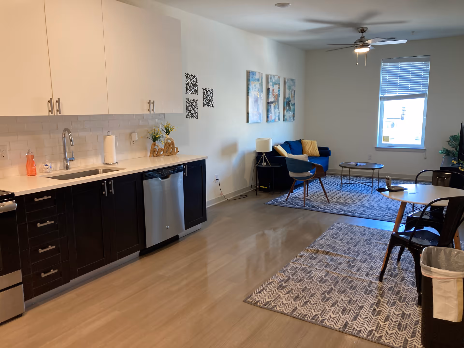 Open-concept kitchenette and living area with sofa, chairs, tables, and cabinets.
