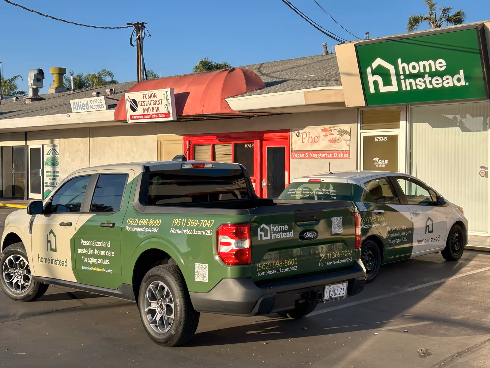 Two Home Instead service trucks parked in front of a strip mall storefront.