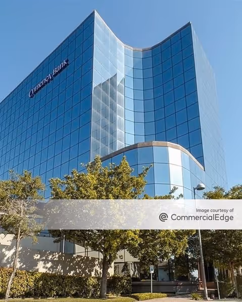 Tall blue-glass building with curved edge, trees, and clear sky.