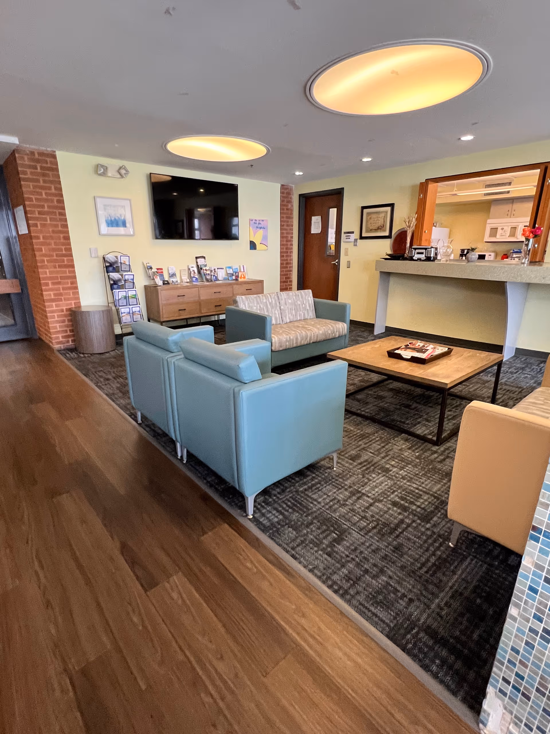 A cozy lounge with teal sofas, a coffee table, and a wall mounted TV.