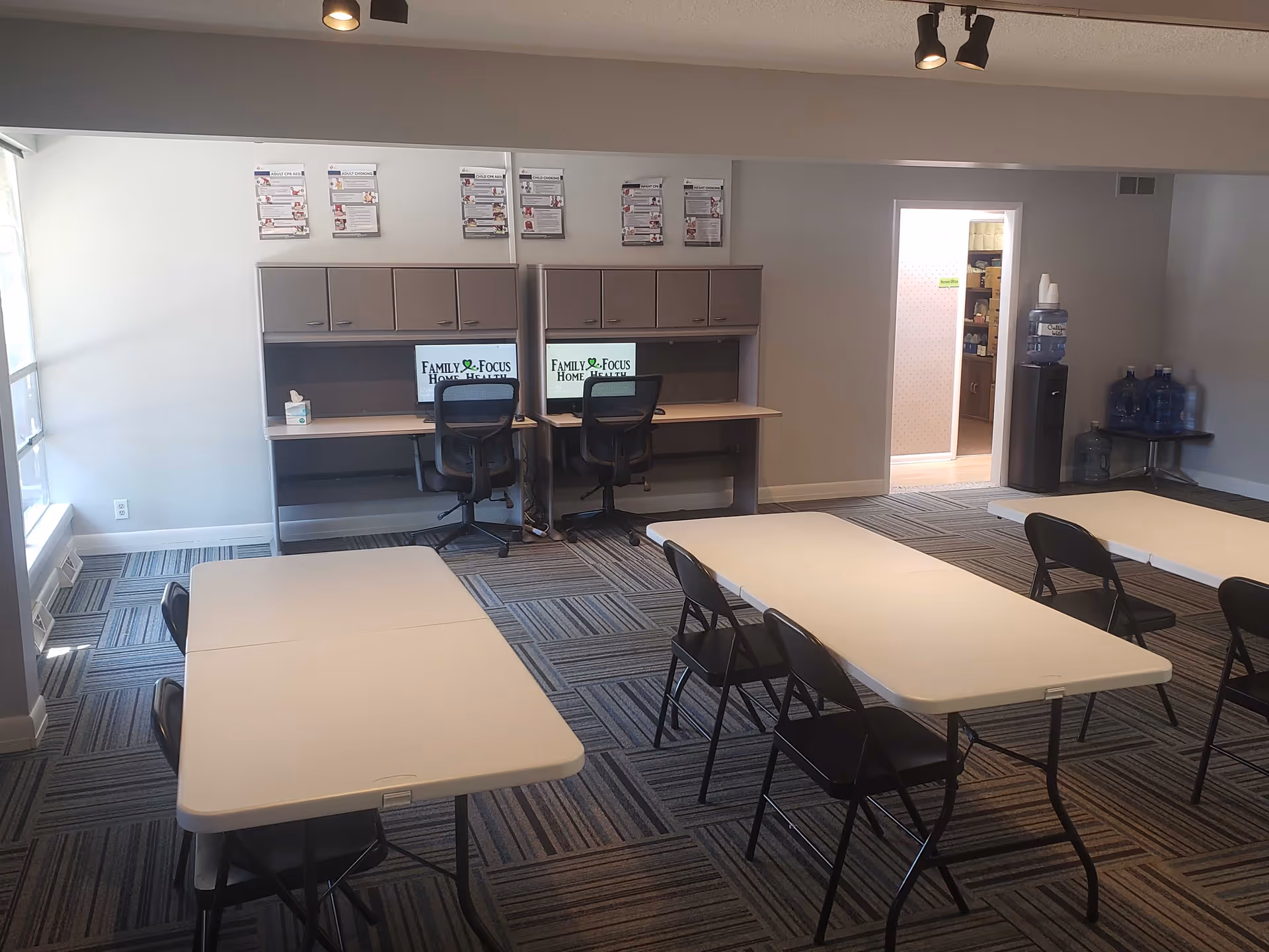A communal room with folding tables, chairs, and two computer desks displaying Family Focus Home Health.