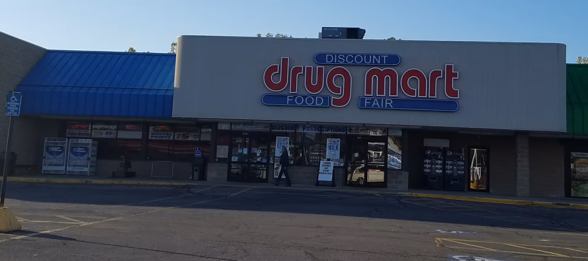 Exterior view of Discount Drug Mart storefront with blue awning and parking lot