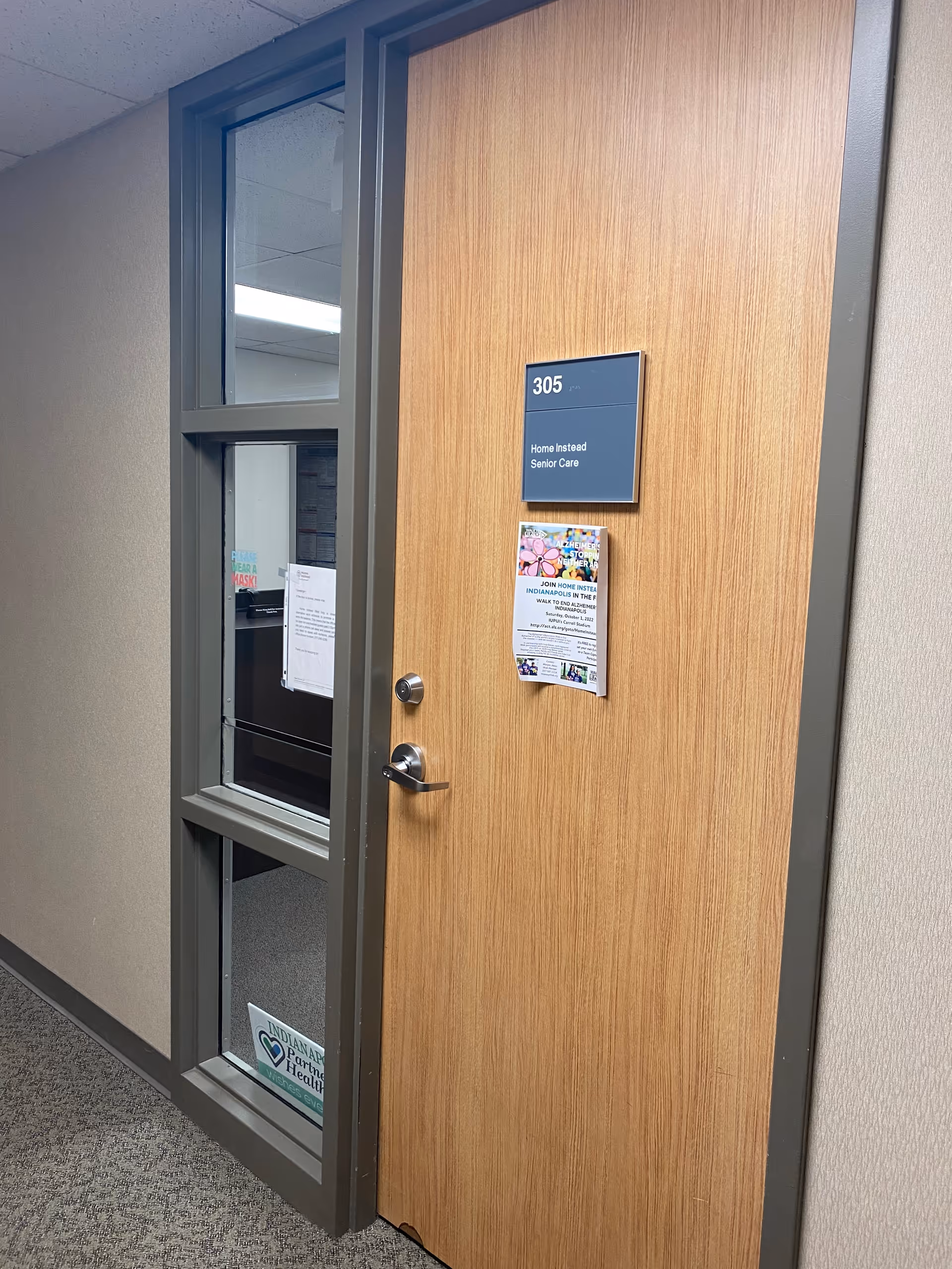 Interior hallway with a wooden door labeled 305 Home Instead Senior Care and posted flyers.