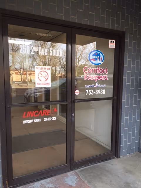 Glass entrance door with Comfort Keepers logo and street address on dark brick building.