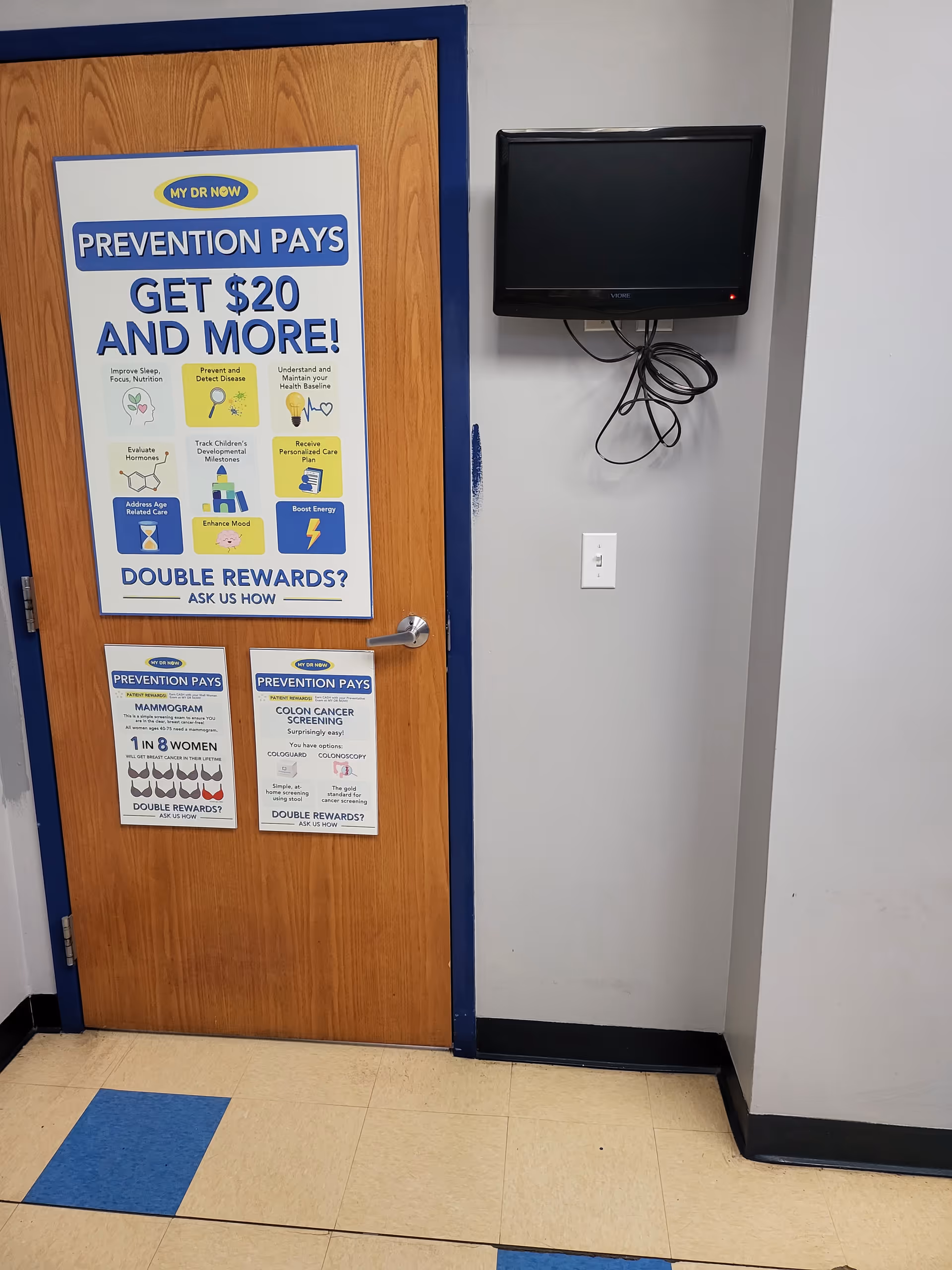 Interior doorway with a wooden door, posters, and a wall-mounted TV with tangled cords.