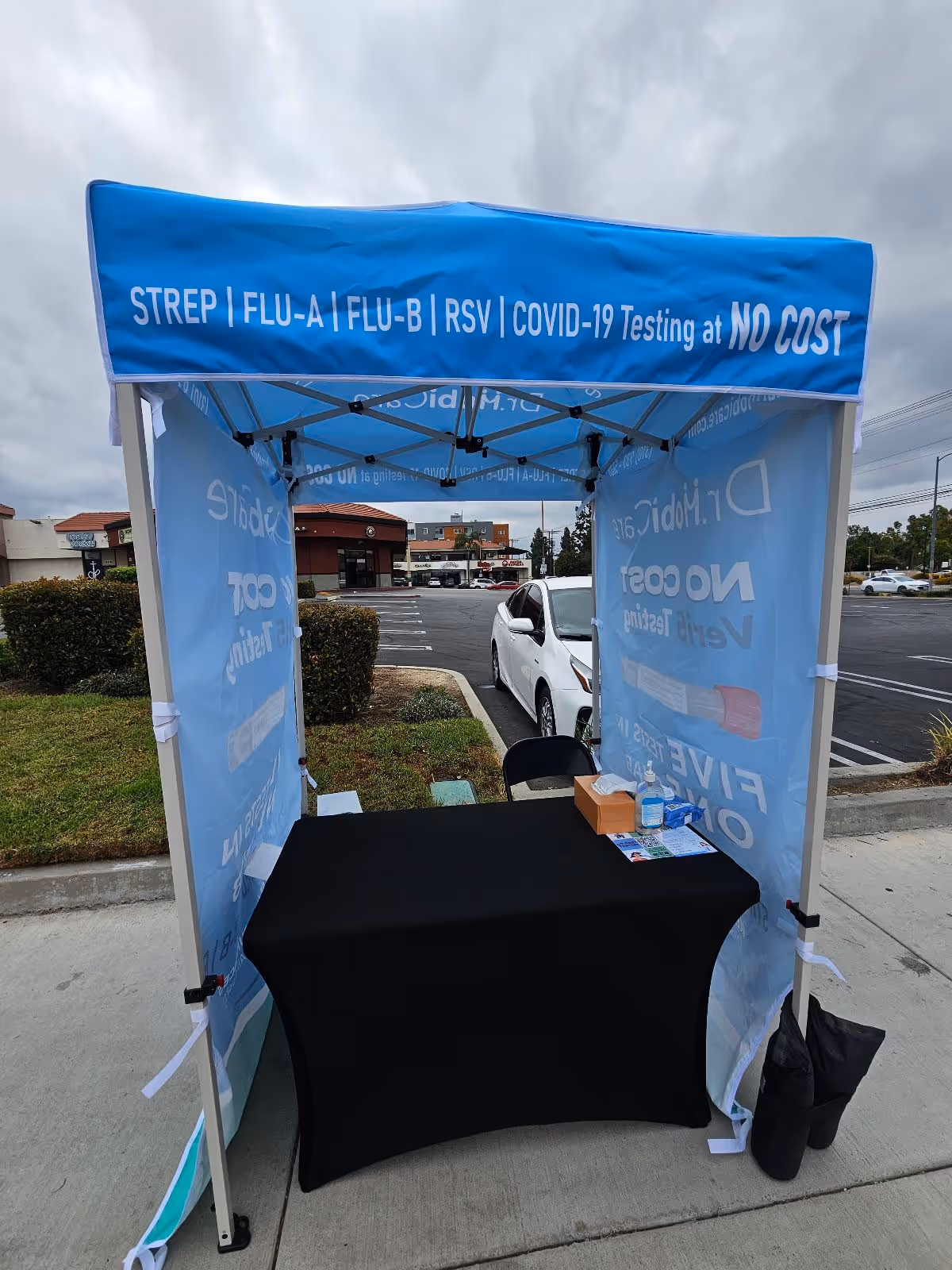 Blue canopy tent provides no-cost flu, RSV, and COVID-19 testing in a parking lot.