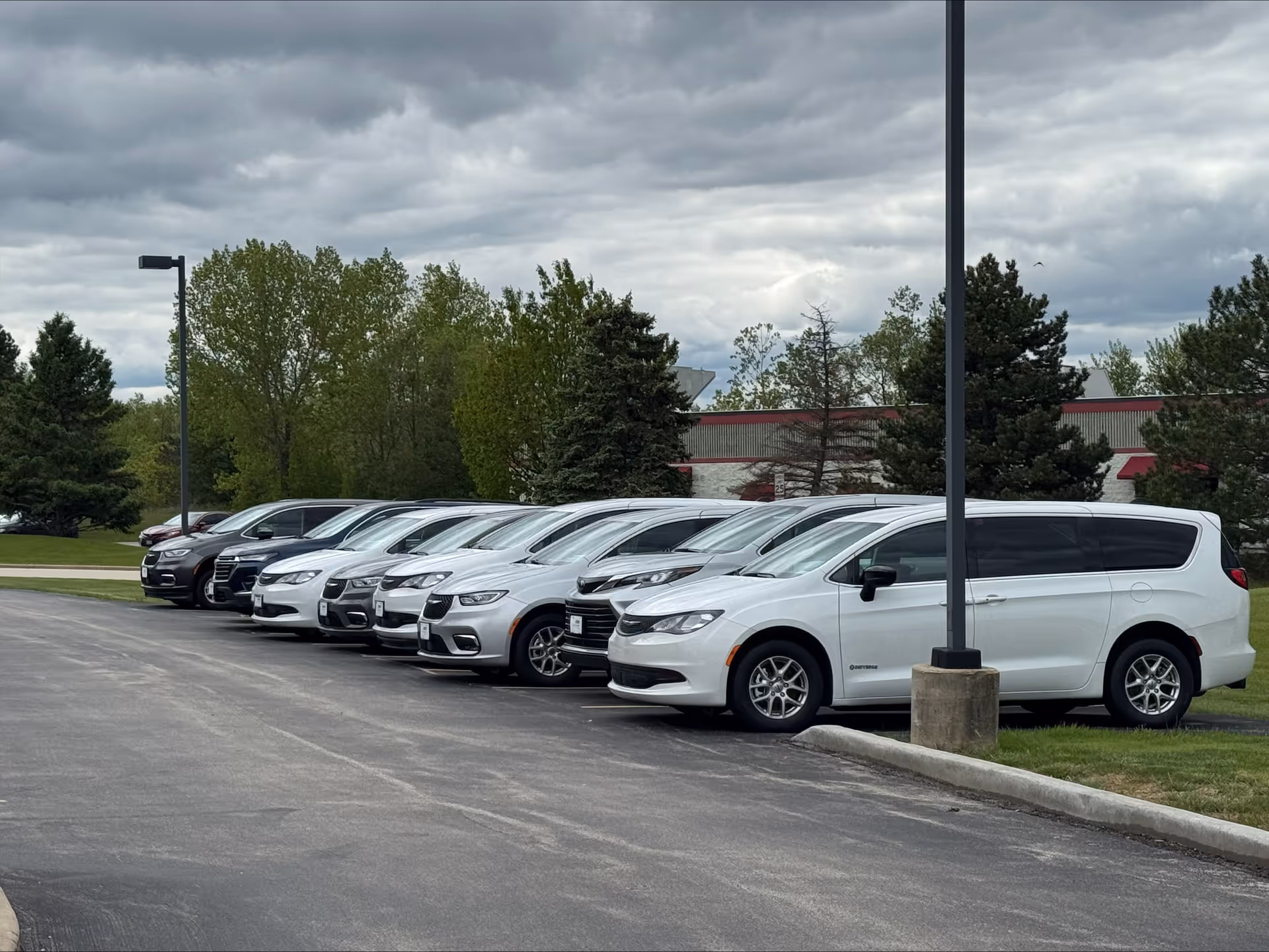 Row of white MobilityWorks vans parked in a facility's exterior lot.