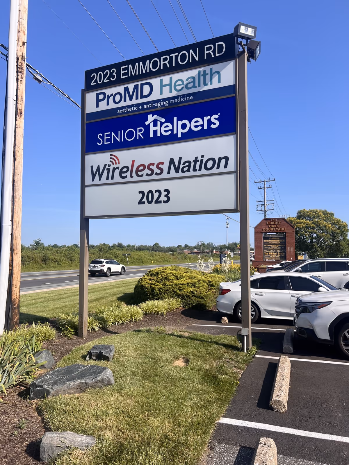 Tall roadside sign shows ProMD Health, Senior Helpers, and Wireless Nation beside parked cars.