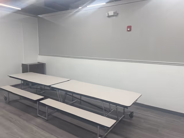 Empty dining room with long tables and benches in a gray-walled interior.
