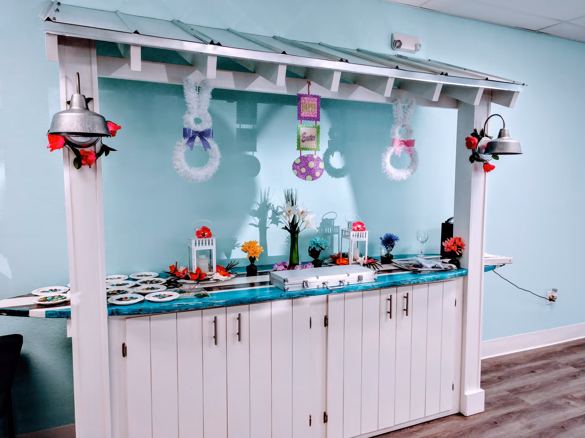 A pastel turquoise dining area buffet with plates, flowers, and decorative wreaths along a counter.