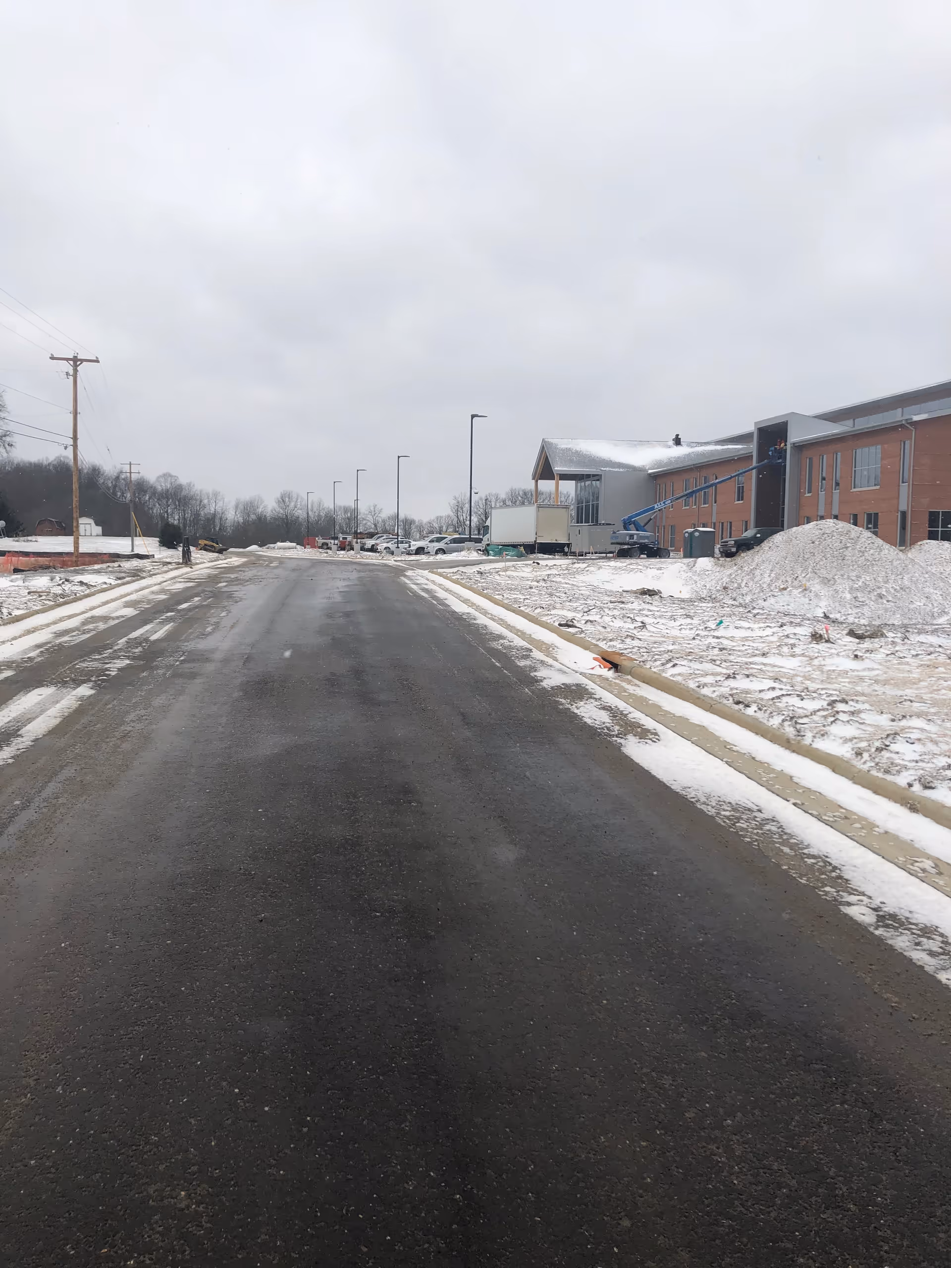 Snowy street view toward a brick facility under construction on the right.
