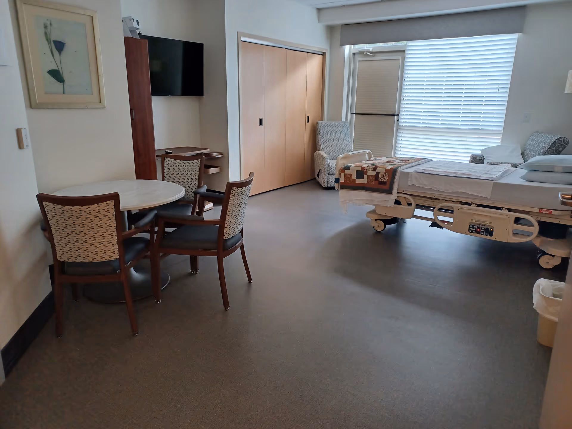 Hospice patient room featuring a bed, table with chairs, TV, and closet.