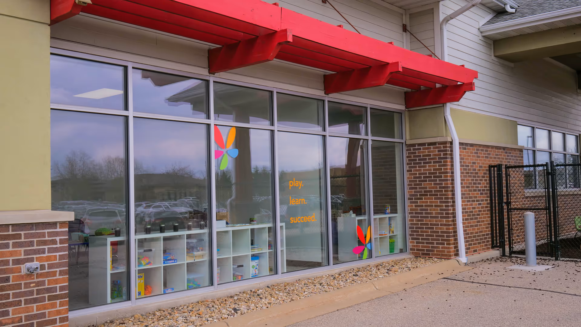 Exterior of a building with large glass windows, a red awning, and brick accents.