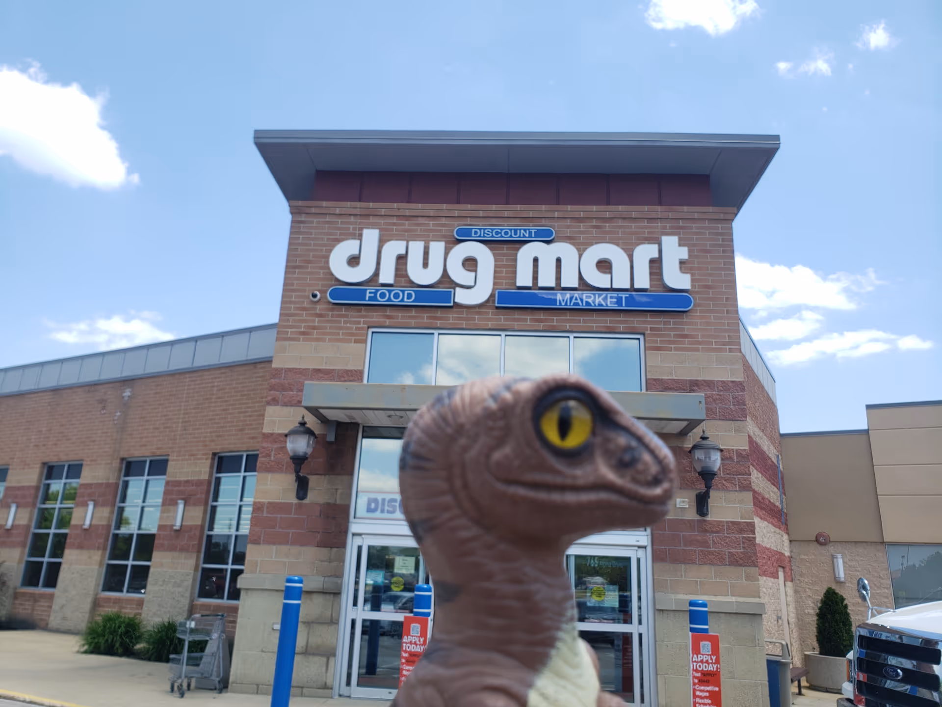 Front of Discount Drug Mart store with a dinosaur toy in foreground.