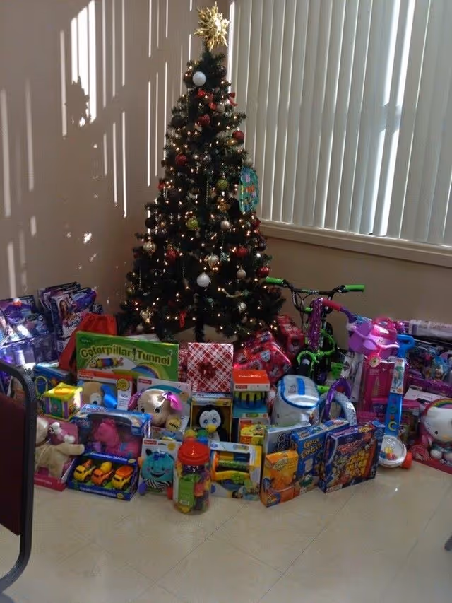 Christmas tree with wrapped gifts and toys inside AGAPE senior living facility.