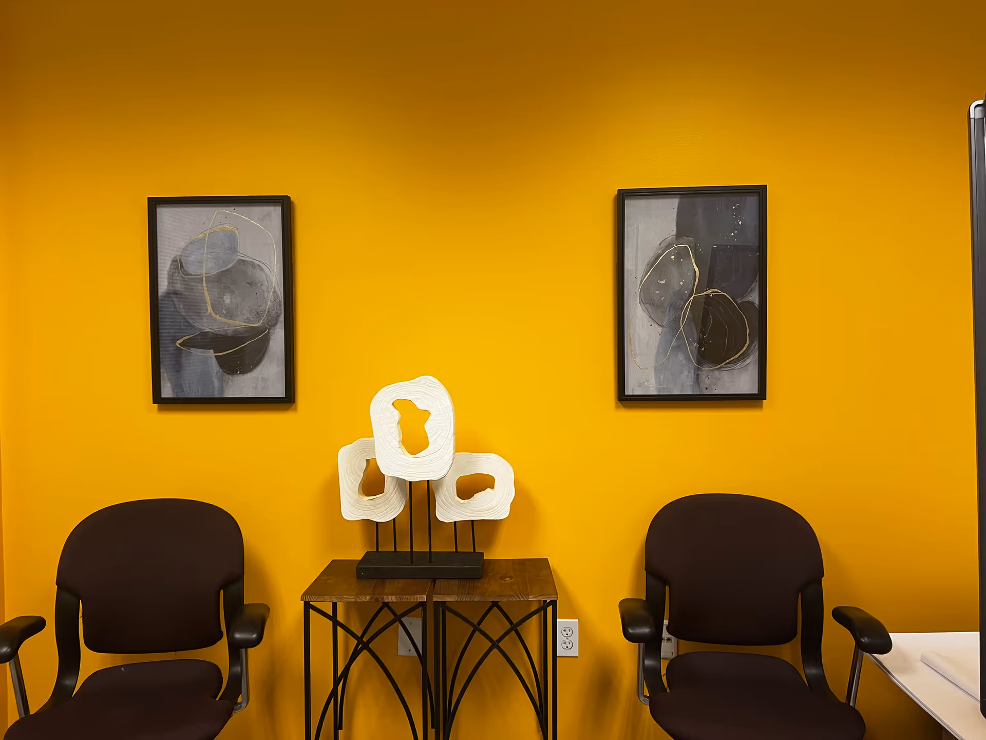 Bright yellow interior featuring abstract art, a wooden console with sculptural decor, and two chairs.