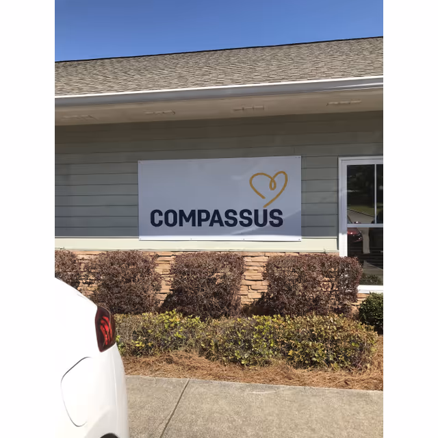 Exterior view of a Compassus facility with sign and shrubs in front.