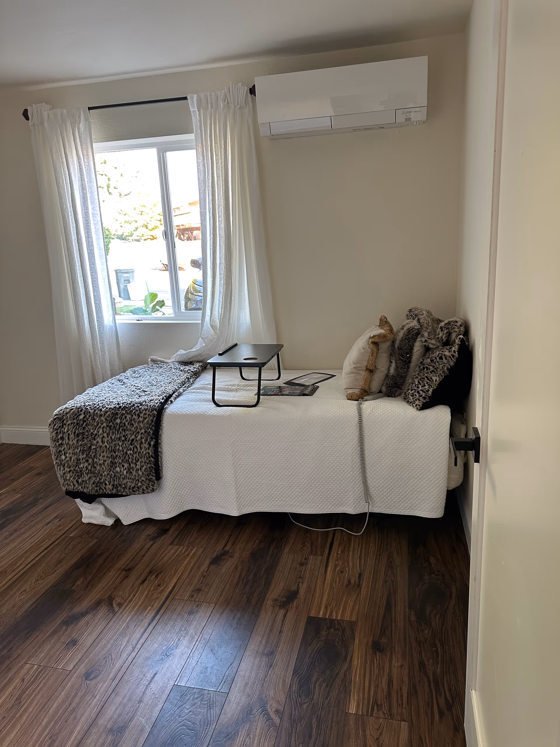 Small bedroom featuring a bed with leopard print throw, pillows, and a window with sheer curtains.