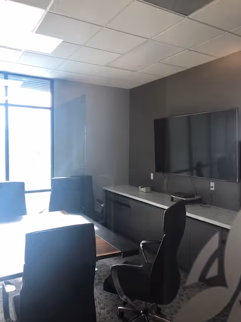 Office-like conference room with wall-mounted TV, table, chairs, and cabinets.