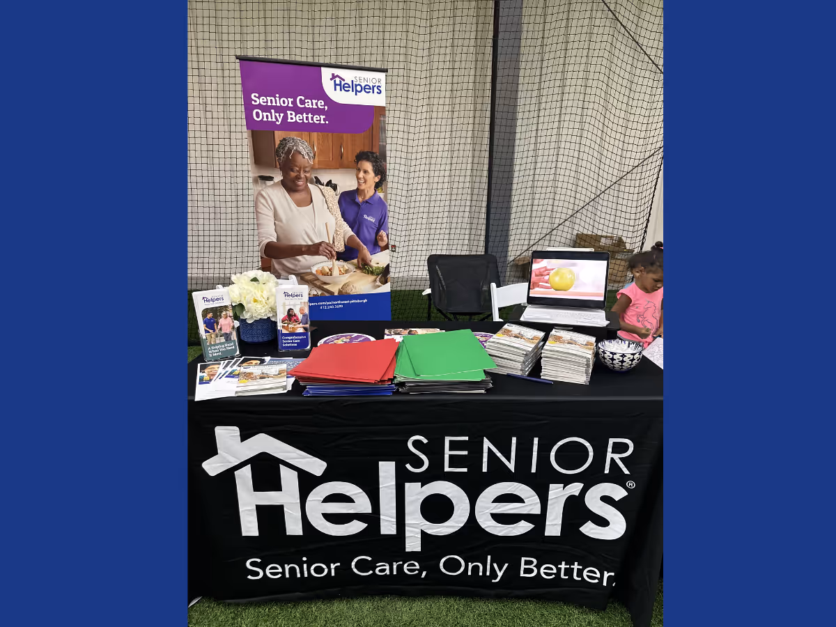 Promotional booth for Senior Helpers featuring banners, brochures, and a staff member.