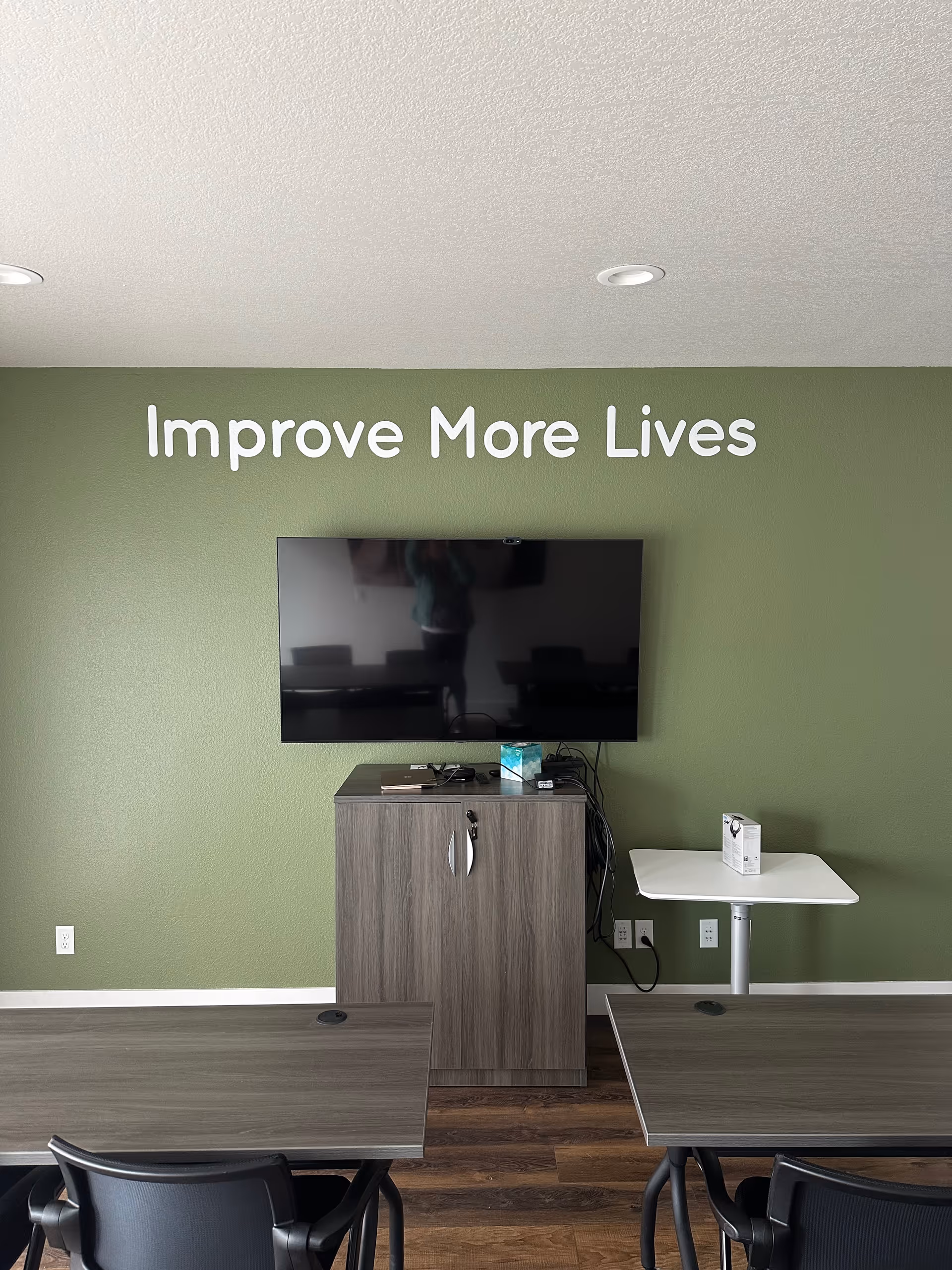 Green-walled lounge area with a mounted TV, cabinet, and dining tables.