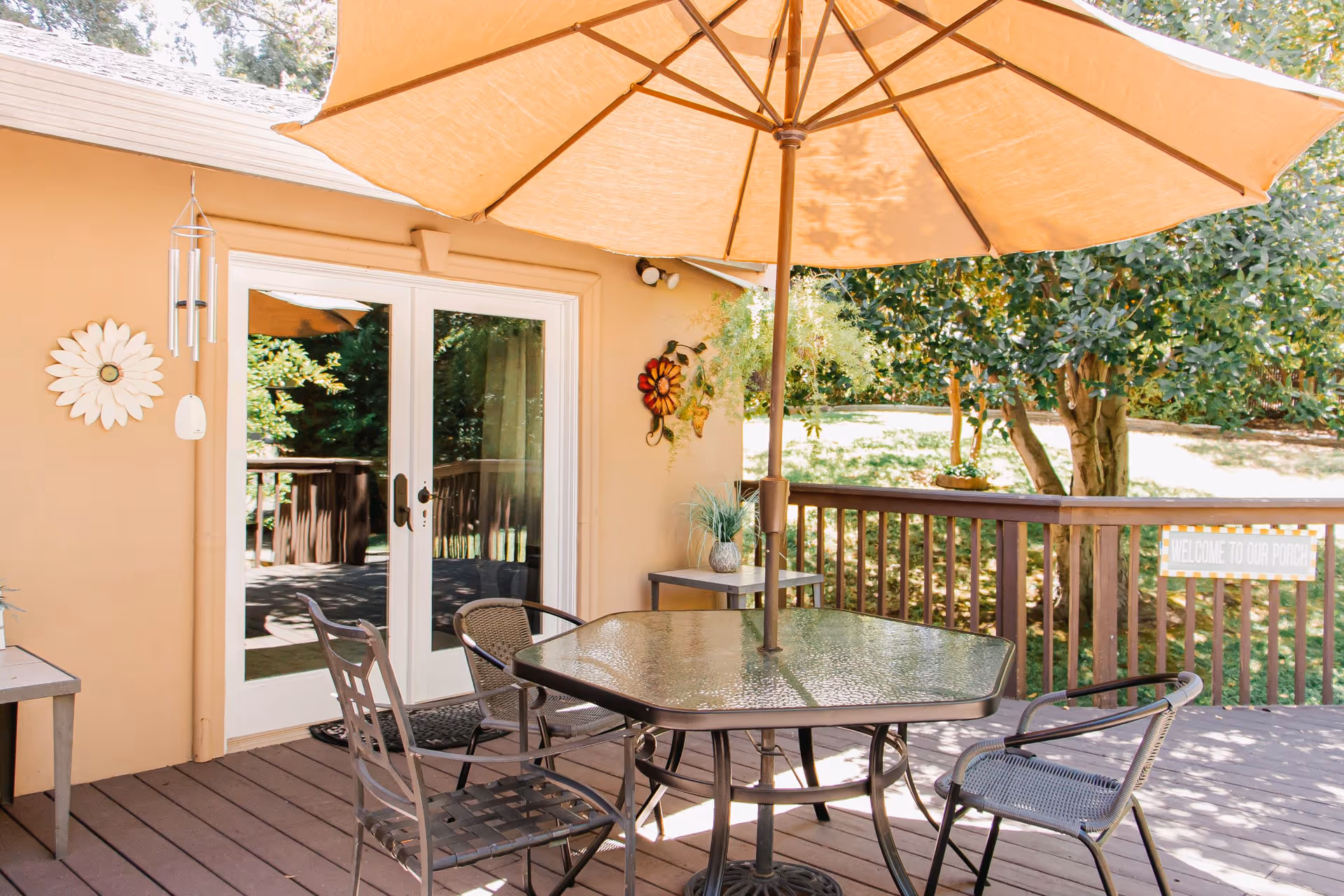 Outdoor patio with glass doors, umbrella, round table, metal chairs, and greenery.