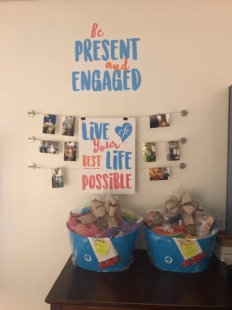 Interior wall with inspirational poster, photo garland, and two gift baskets on a table.